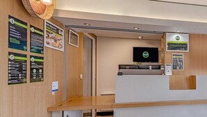 A hotel reception area with a wooden reception desk, a flat-screen TV, and informational posters on the walls. - B&B HOTEL Brest Kergaradec (Gouesnou)