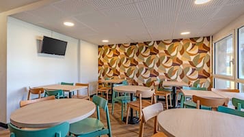 Un espace repas moderne avec des tables et des chaises rondes, un mur décoré de motifs et un téléviseur fixé au mur.
