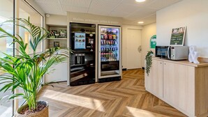 A kitchenette area with a microwave, a refrigerator, and a vending machine. - B&B HOTEL Brest Kergaradec (Gouesnou)