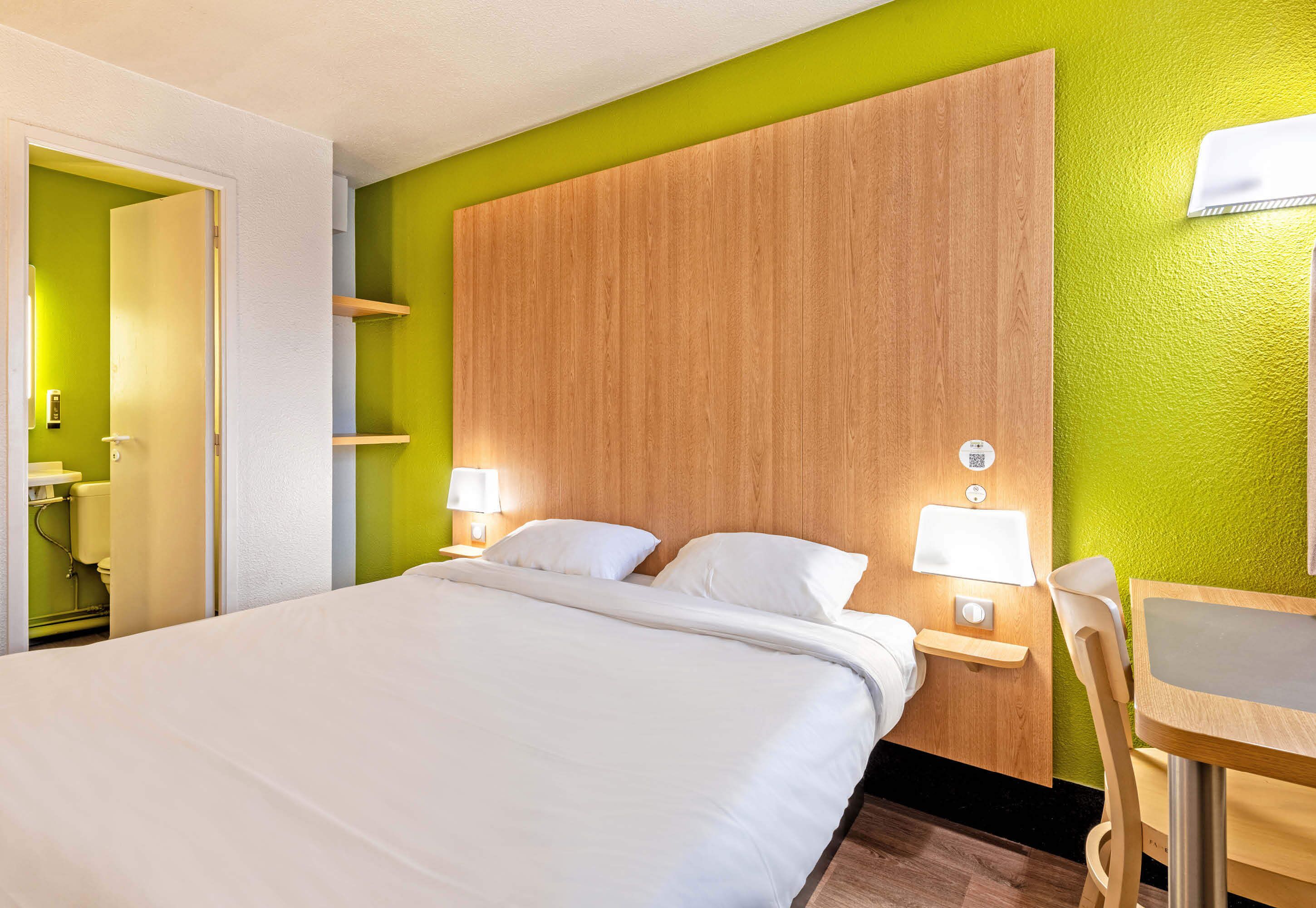 Una habitación de hotel con una cama grande, mesitas de noche con lámparas, un cabecero de madera y una pared de acento verde.
