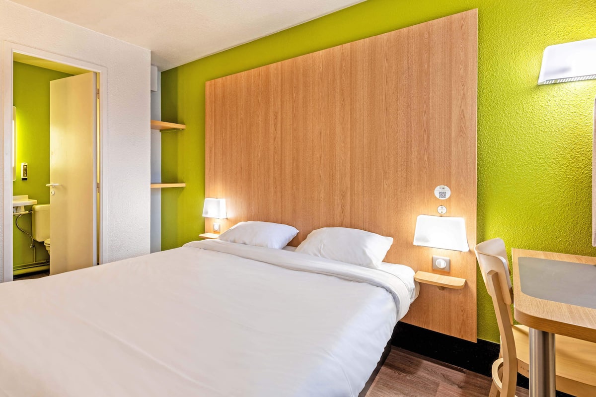 A hotel room with a large bed, bedside tables with lamps, a wooden headboard, and a green accent wall.