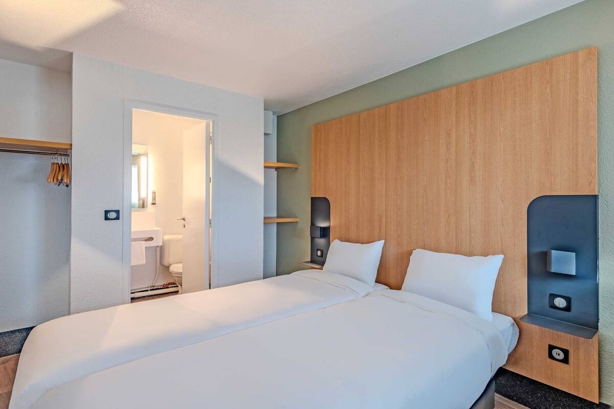 A modern hotel room with a large bed, wooden headboard, bedside tables, and a visible bathroom.