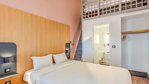 A modern hotel room with a large bed, a wooden headboard, a staircase leading to an upper level, and a bathroom visible through an open door. - B&B HOTEL Brest Kergaradec (Gouesnou)