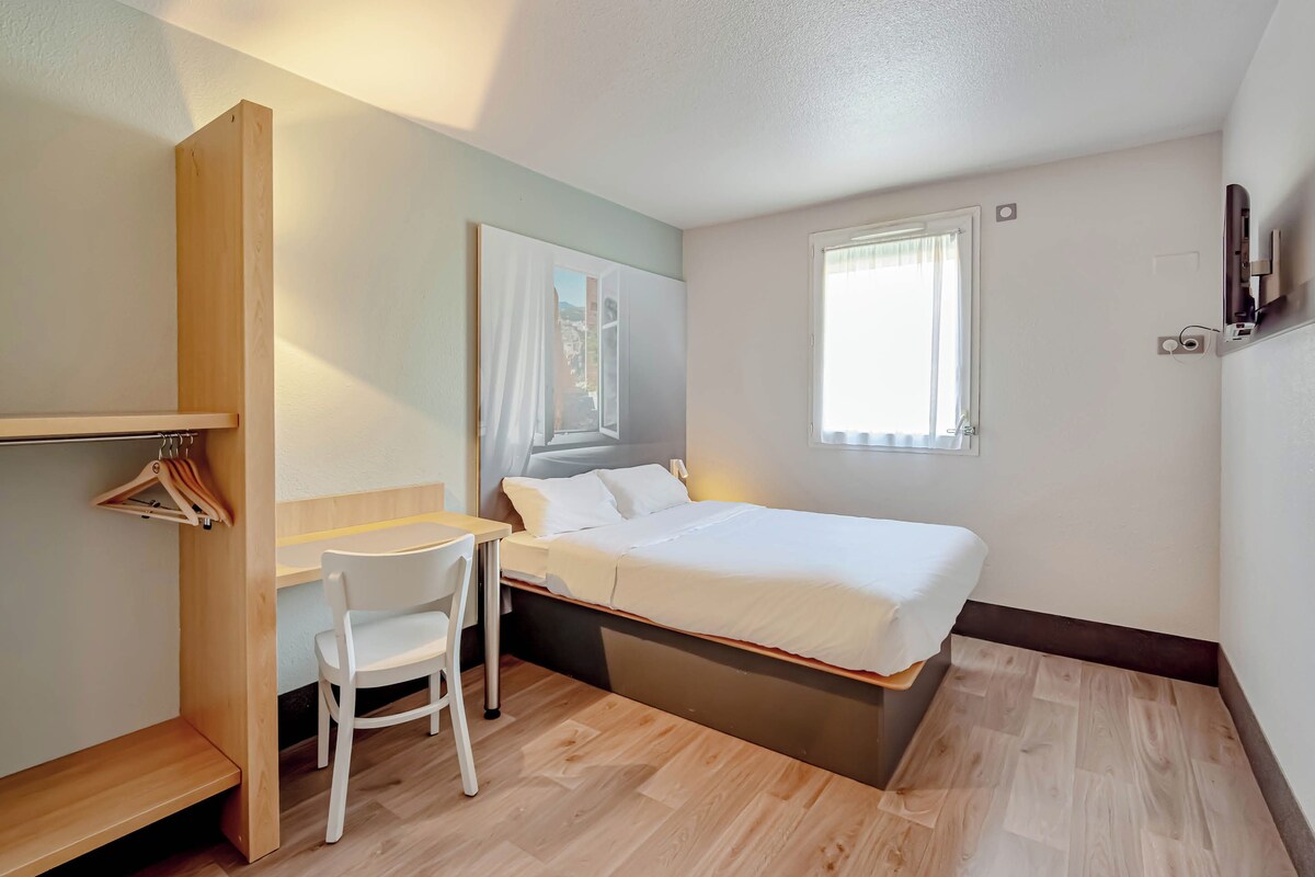 Een kleine slaapkamer met een bed, een bureau, een stoel en een kledingkast.