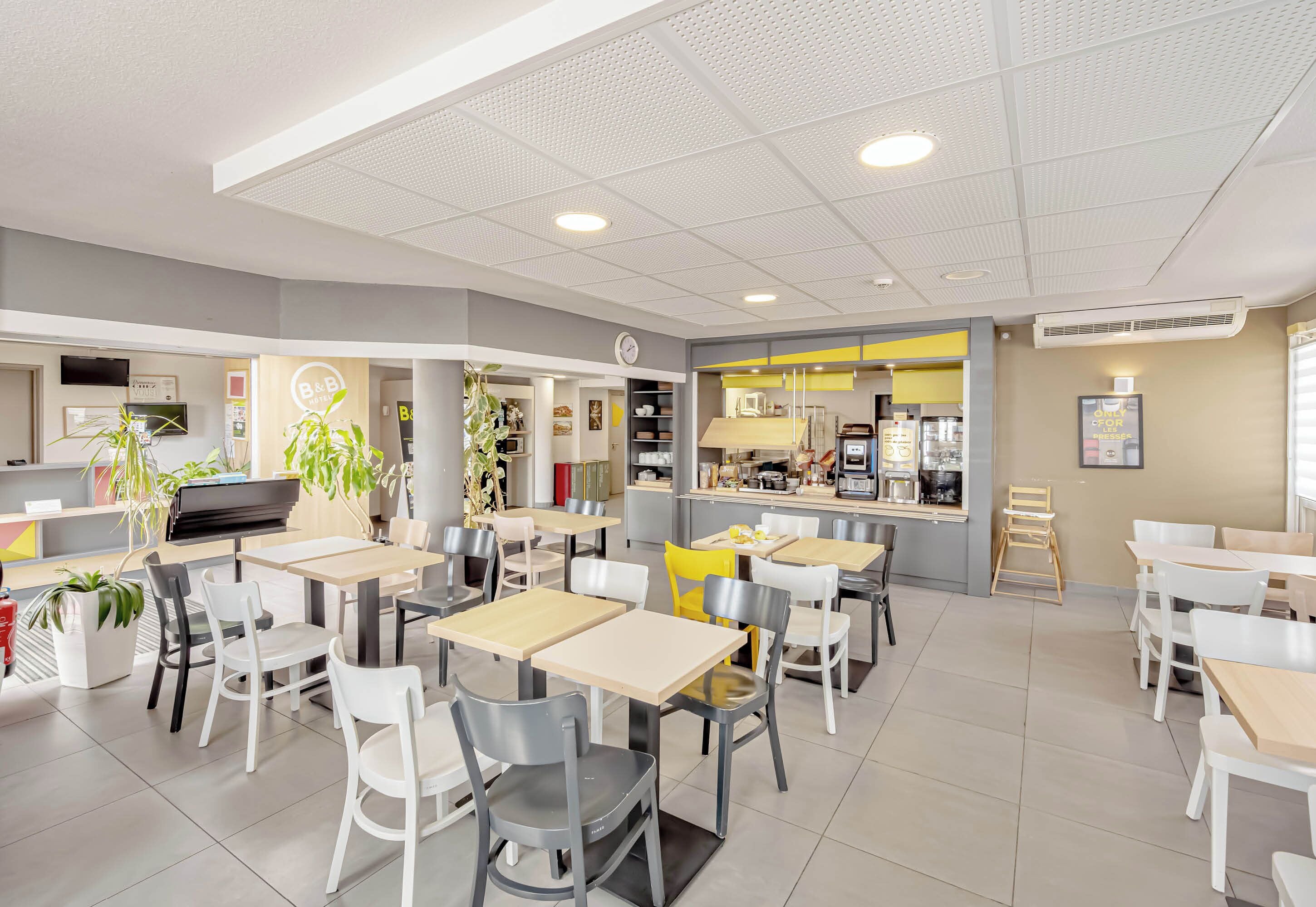 Un café moderne avec de nombreuses tables et chaises, un espace cuisine et une horloge au mur.