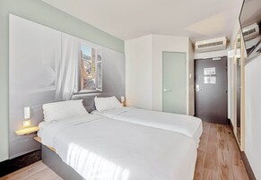 Un dormitorio moderno con cama, mesitas de noche, una ventana con cortinas, una puerta y un equipo de aire acondicionado.