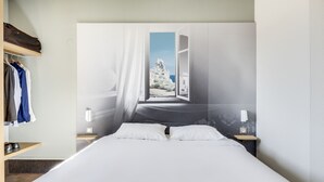 Quarto com cama, guarda-roupa, mesa de cabeceira e luminária na parede.