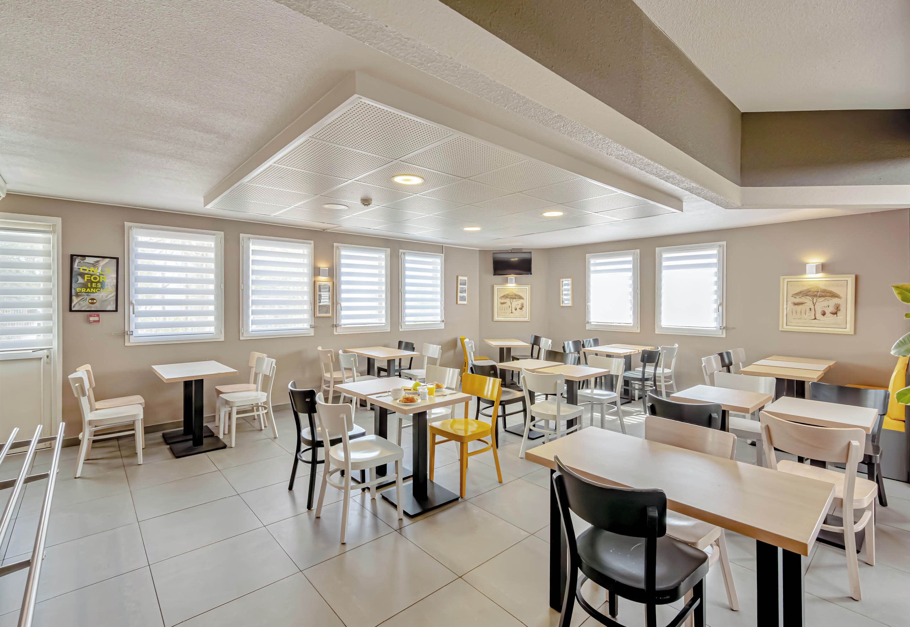 A spacious dining area with multiple tables and chairs, ceiling vents, and framed pictures on the walls.