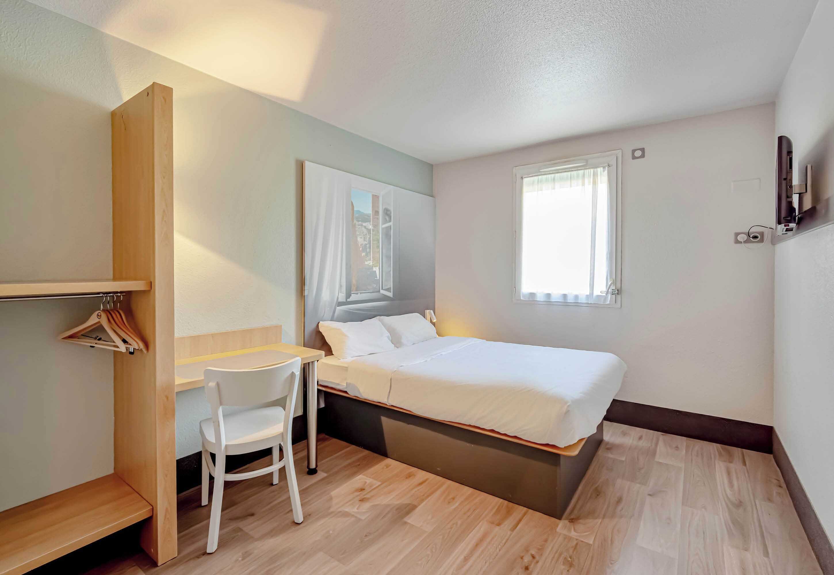 A bedroom with a bed, a desk, a chair, a wardrobe, and a window.