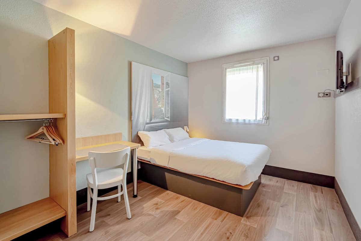 A compact bedroom with a bed, a desk, a chair, and a wardrobe.