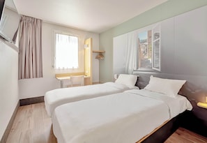 Habitación de hotel con dos camas, un escritorio, una silla y una ventana con cortinas.