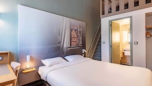 Een hotelkamer met een groot bed, een nachtkastje met een lamp, een kunstwerk aan de muur, een trap en een badkamer zichtbaar door een geopende deur.