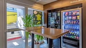 Een modern interieur met een houten tafel, een automaat gevuld met snacks en dranken, en een potplant.