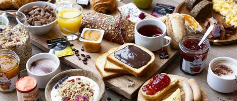 Variedad de alimentos para el desayuno, como cruasanes, queso y frutas, sobre una mesa de madera.