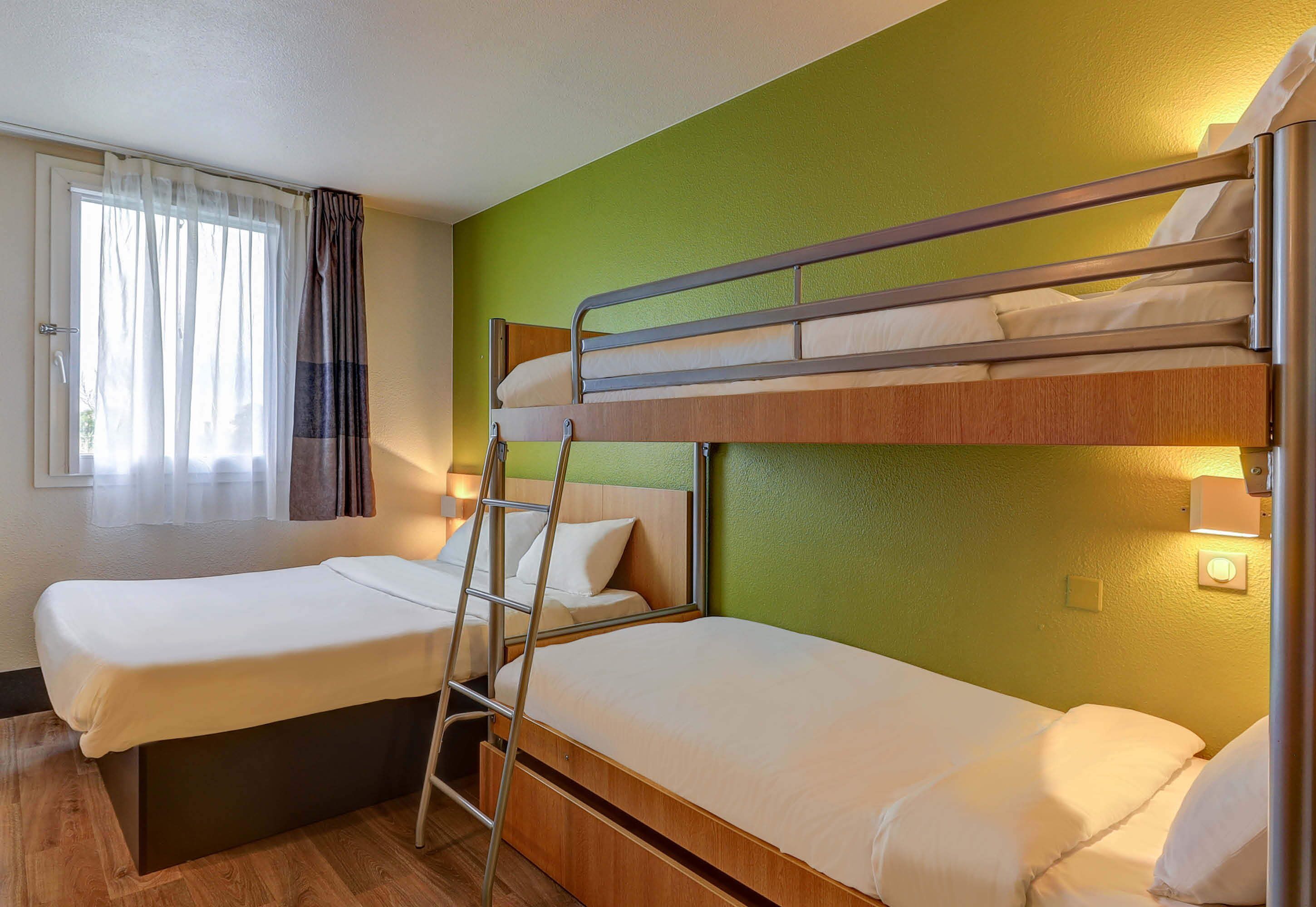 A bunk bed room with a window, curtains, and a bedside lamp.