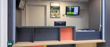 A reception area with a desk, a computer, and a wall-mounted screen.