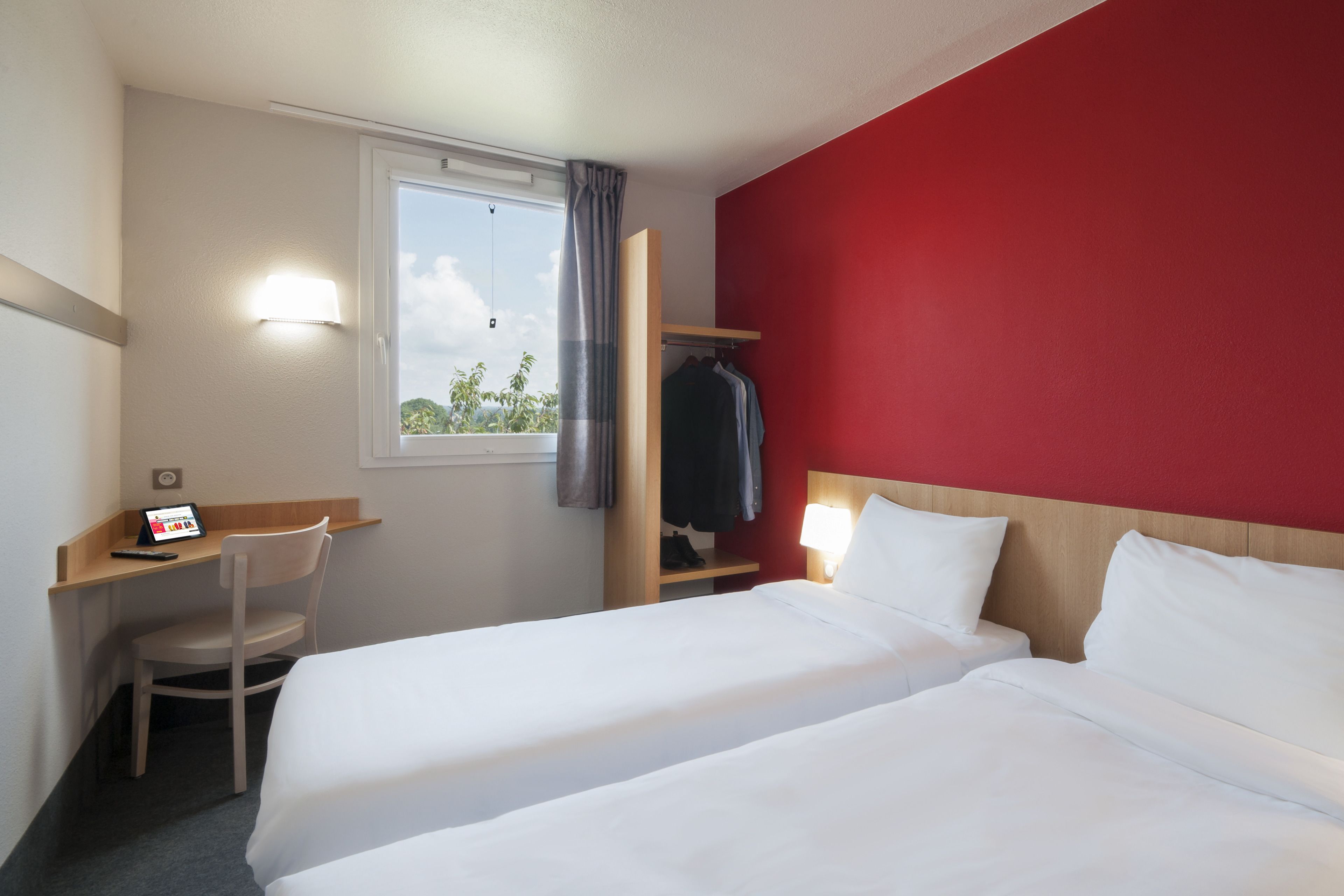 Una habitación de hotel con dos camas, un escritorio, una silla, un armario y una ventana con cortinas.