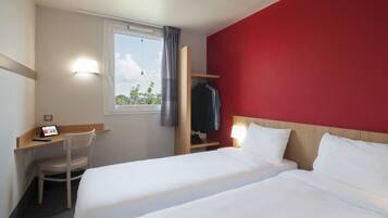 Una habitación de hotel con dos camas, un escritorio, una silla, un armario y una ventana con cortinas.