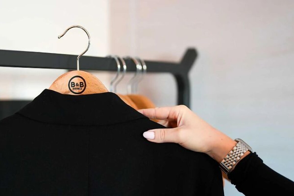 Een hand houdt een zwart kledingstuk op een houten kleerhanger met een etiket.
