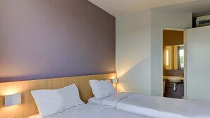 Une chambre d’hôtel avec un grand lit, deux tables de chevet, une petite table et une salle de bain visible à travers une porte ouverte.