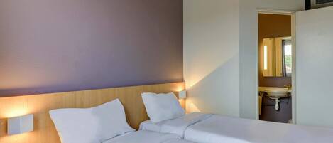 A hotel room with a large bed, two bedside tables, a nightstand, and a bathroom visible through an open door.