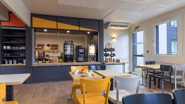 Un café moderne avec un comptoir central, un espace salon et une cuisine située à l’arrière.