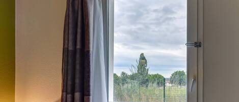 A window with a view of trees and a cloudy sky.