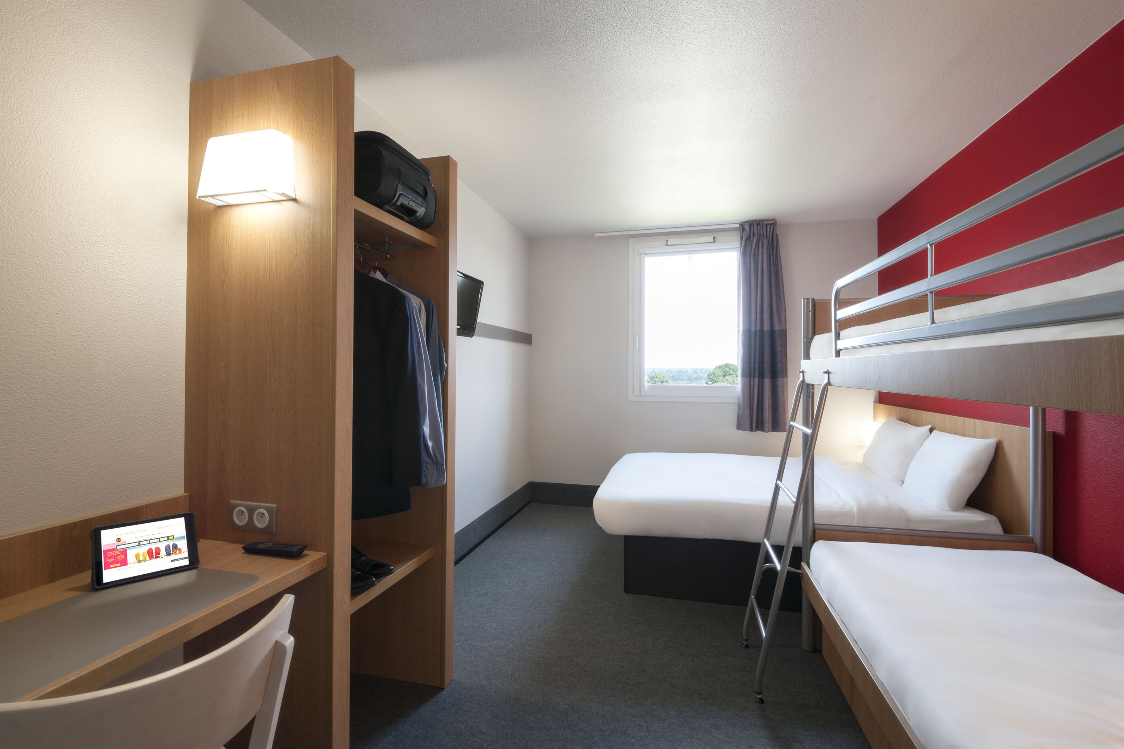 Habitación de hotel con escritorio, dos camas, armario y ventana con cortinas.