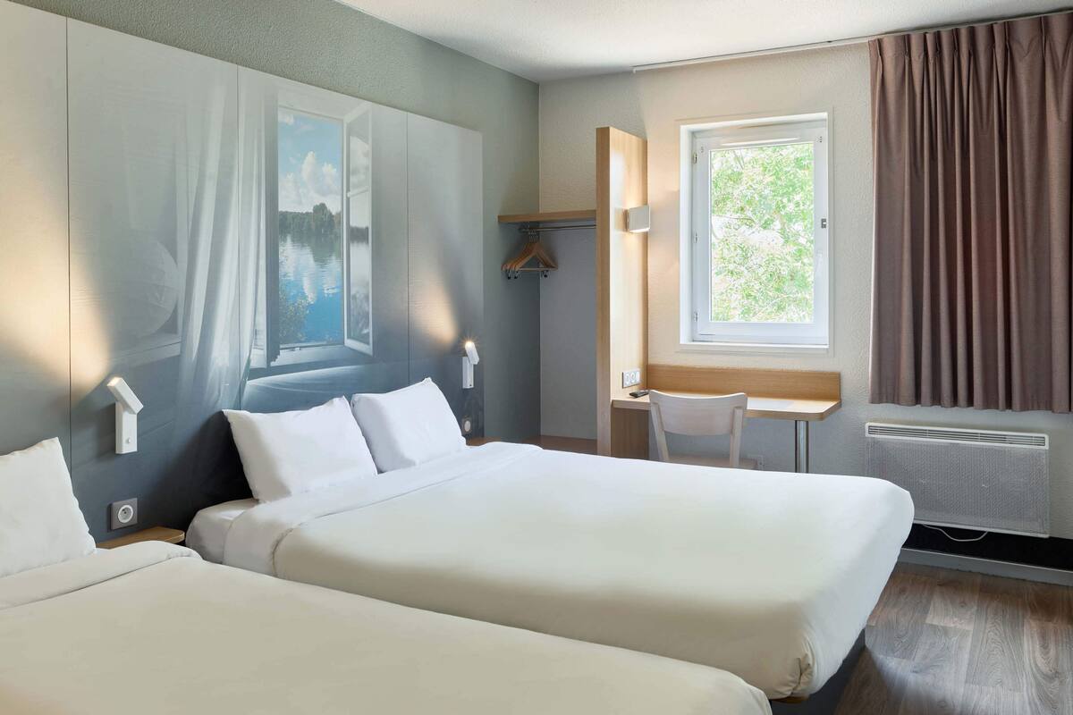 Une chambre d’hôtel avec deux lits, un bureau, une chaise et une fenêtre avec des rideaux.