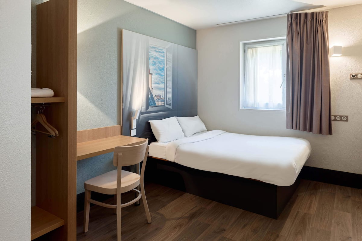Une chambre d’hôtel de taille réduite, comprenant un lit simple, un bureau et une chaise.