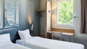 Een hotelkamer met twee bedden, een bureau en een stoel. Er is een raam met uitzicht op groen.