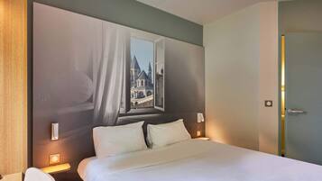 Habitación de hotel con una cama grande, dos mesitas de noche con lámparas, vista a un edificio por la ventana y una puerta a la derecha.