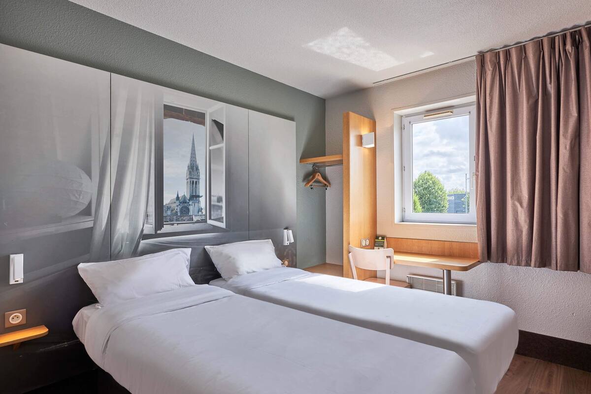 A hotel room with a large bed, a desk, and a view of a cityscape through the window.