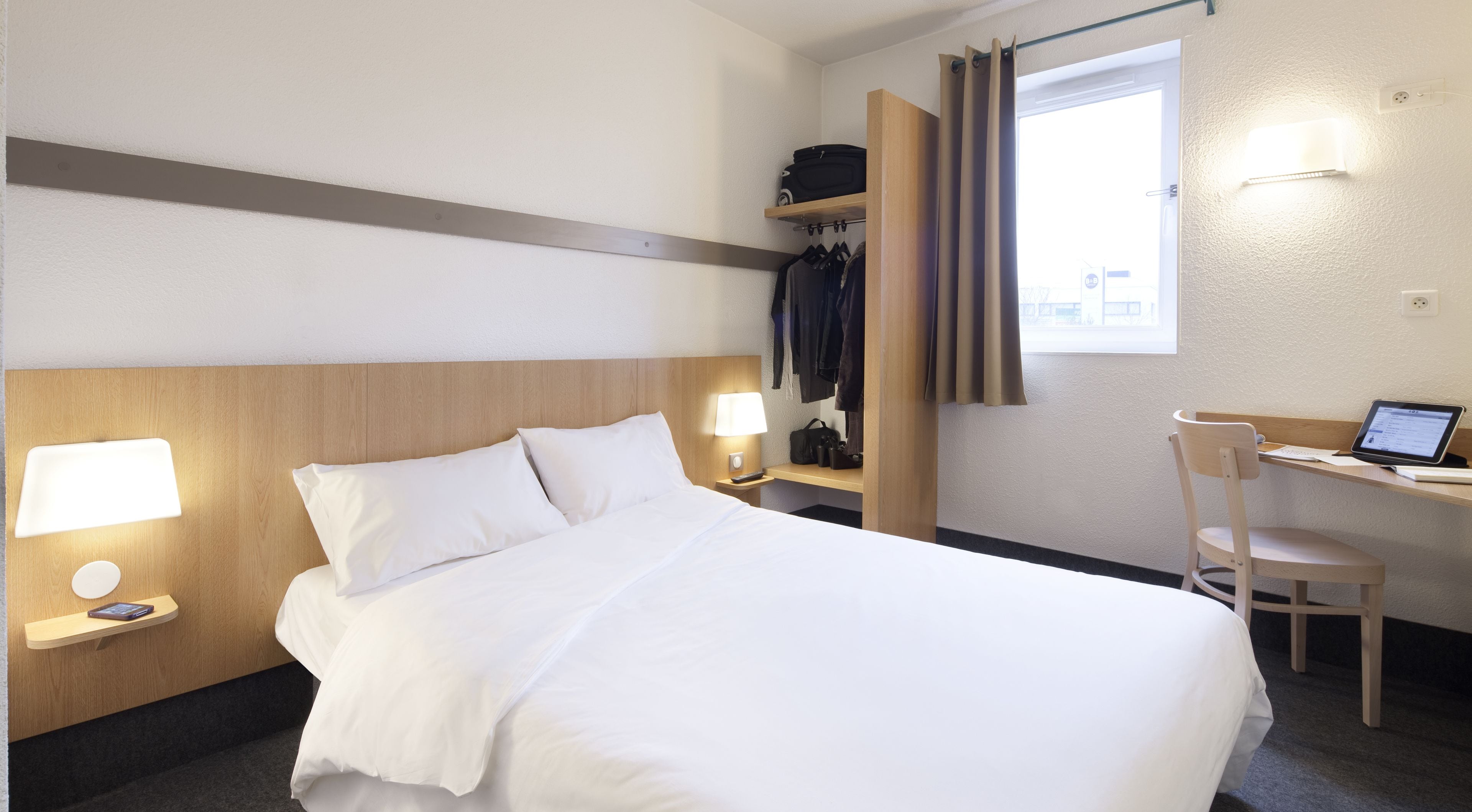 Une chambre d’hôtel comprenant un lit, des lampes de chevet, un bureau avec un ordinateur portable, une chaise et une armoire.