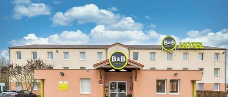 A B&B hotel with a simple facade, a central entrance, and a parking area in front.