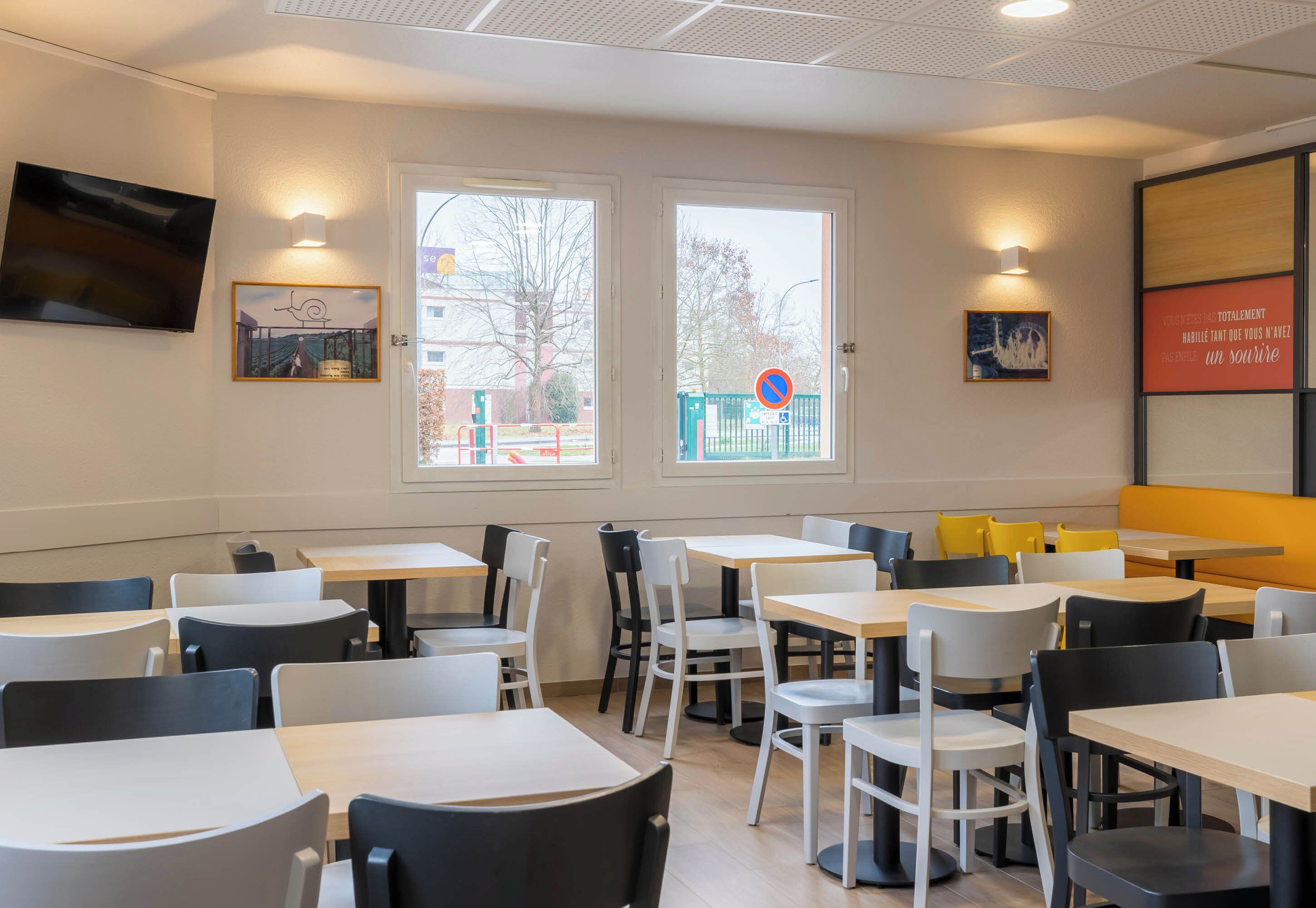 A restaurant with multiple tables and chairs, large windows with a view of the outside, and wall-mounted artwork.