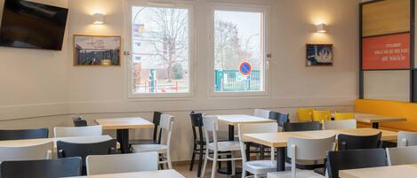 A restaurant with multiple tables and chairs, large windows with a view of the outside, and wall-mounted artwork.