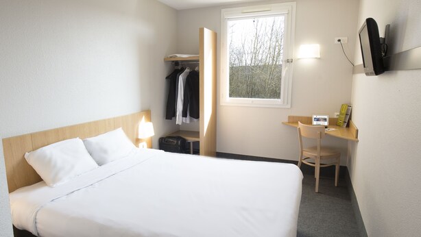 Una habitación de hotel con cama, escritorio, silla, armario y ventana.