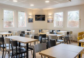 A dining area with multiple tables and chairs, large windows, and a flat-screen TV mounted on the wall.