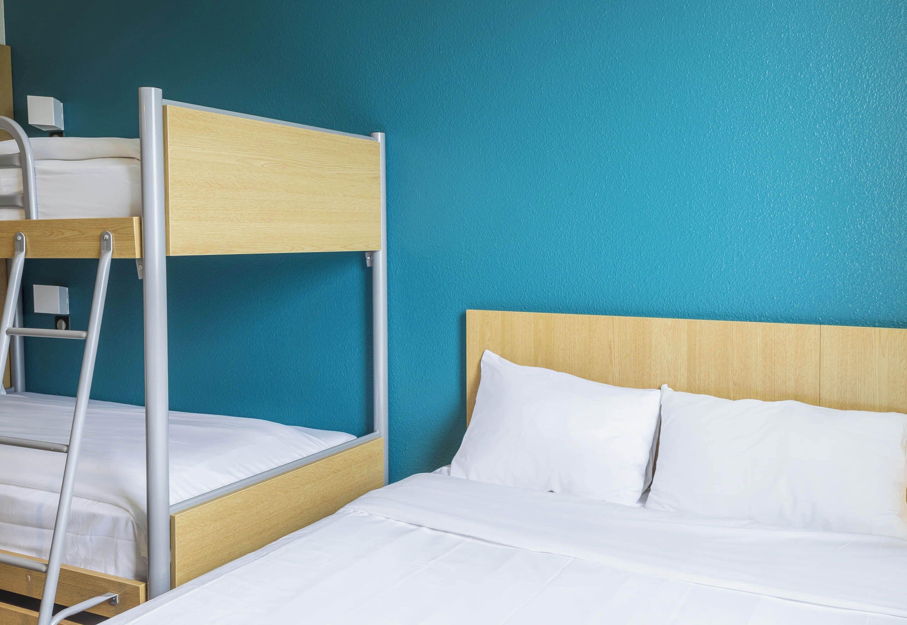 A bunk bed with a wooden headboard and white bedding, set against a teal wall.
