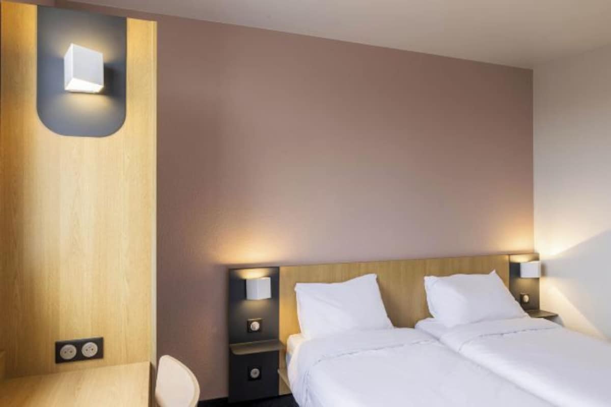 A hotel room with a bed, bedside tables, and a wall-mounted light fixture.