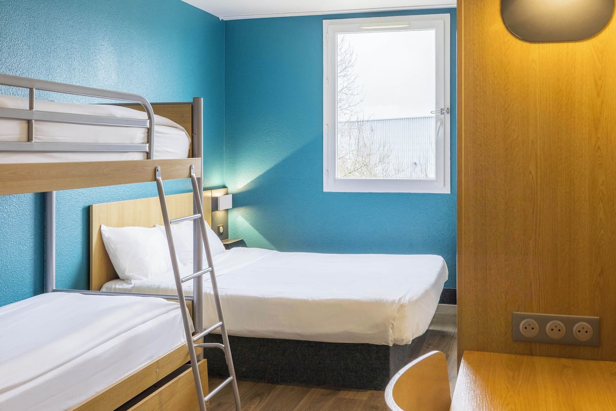 A room with two single beds, a bunk bed, a wooden desk, a chair, a window, and a wall socket.