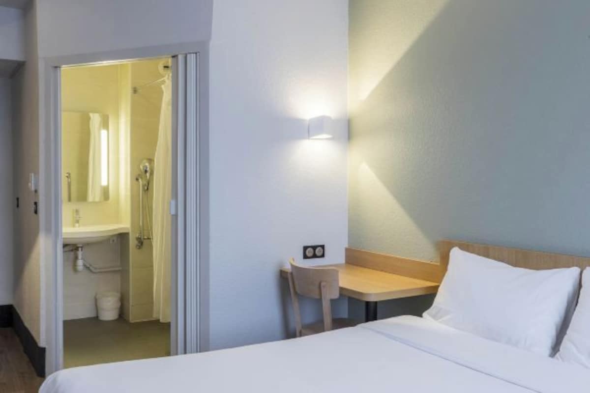 A hotel room with a bed, a desk, and a bathroom visible through an open door.