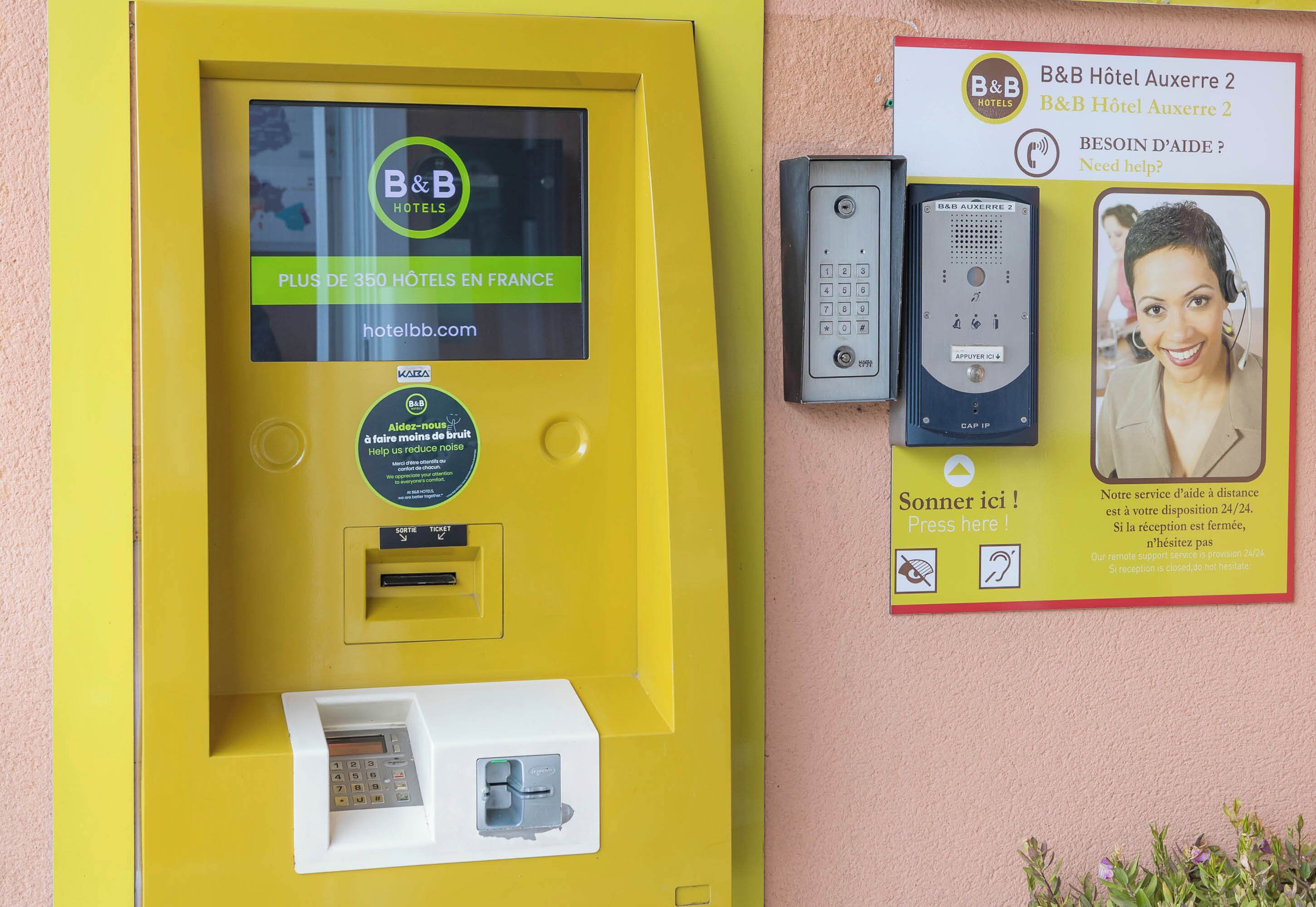 Quiosco amarillo de autoservicio para un hotel, con una pantalla que muestra el logotipo de B&B Hotels y una dirección web.