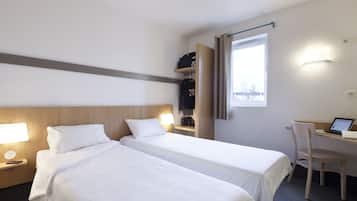 A hotel room with two beds, a desk with a laptop, a chair, and a window with curtains.