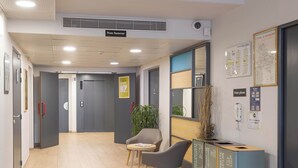 Un área de recepción con un mostrador, dos sillas, una planta en maceta y carteles informativos en la pared.