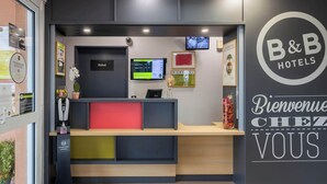 Una recepción con una pantalla digital, un letrero que dice 'Privé' y un cartel en la pared que dice 'Bienvenue Chez Vous'.