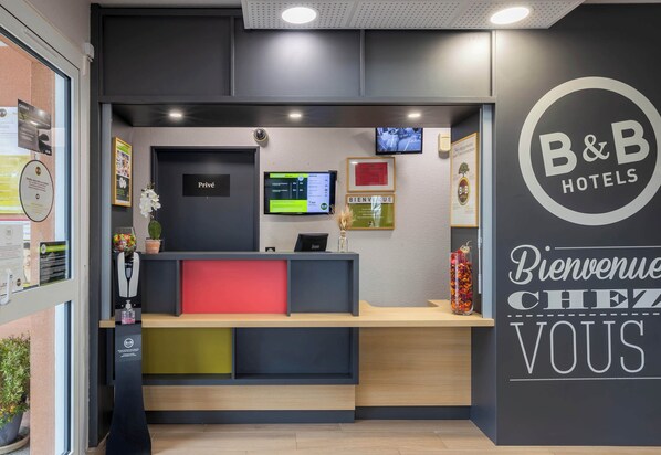 Una recepción con una pantalla digital, un letrero que dice 'Privé' y un cartel en la pared que dice 'Bienvenue Chez Vous'.