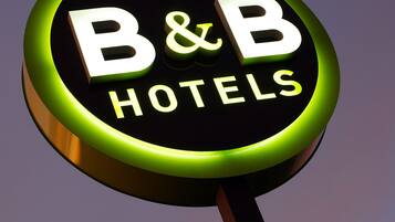 Pyöreä kyltti, jossa lukee ”B&B HOTELS”, ja taustalla violetti taivas.