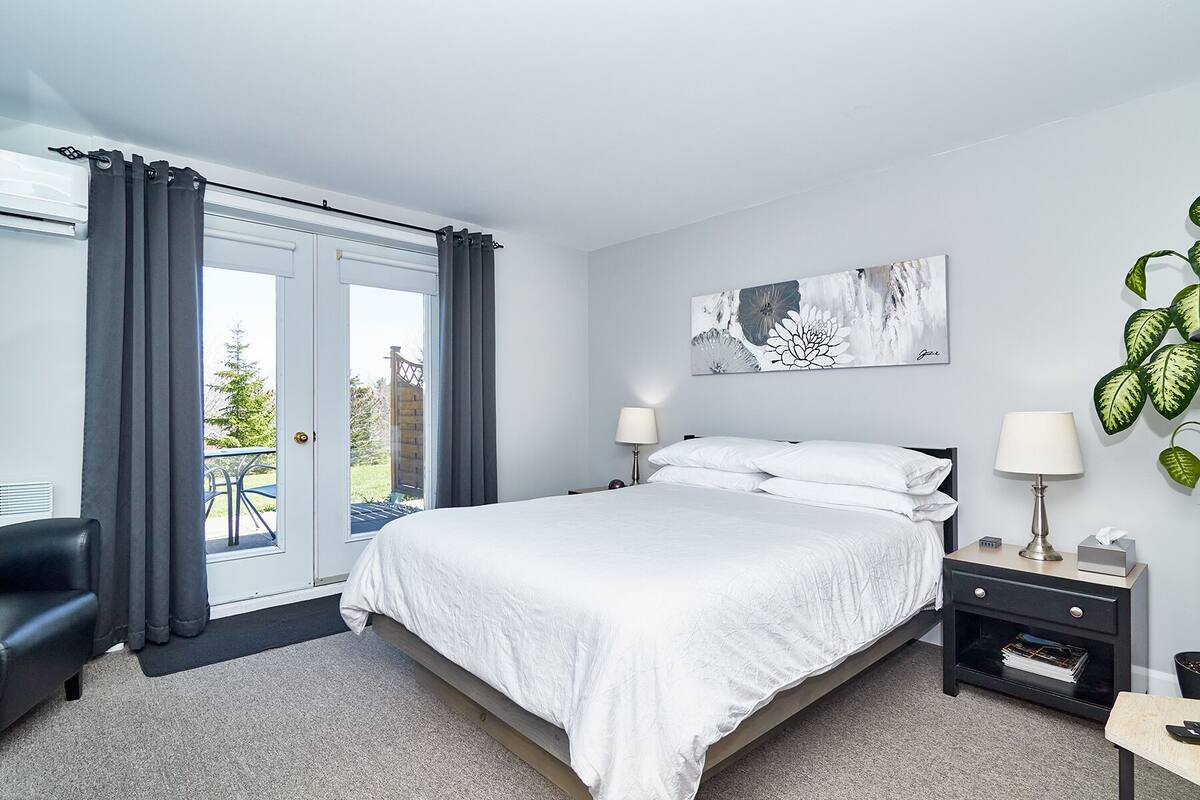 Une chambre à coucher comprenant un lit, deux tables de chevet, une commode, une fenêtre avec des rideaux et une vue sur l’extérieur.